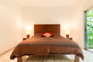 Une chambre moderne avec un grand lit, deux lampes de chevet et une vue sur la verdure grâce à une grande fenêtre.