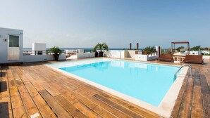A rooftop pool with wooden decking, lounge chairs, and potted plants.