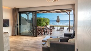 Een moderne woonkamer met een grote schuifdeur naar een terras met tuinmeubels en uitzicht op zee.