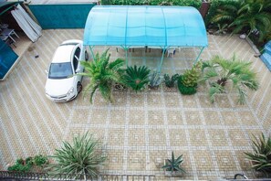 A tiled patio with a car and a covered structure, surrounded by various plants. - Renessans (Sirius)