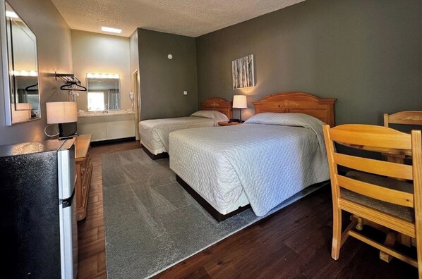 A hotel room with two beds, a desk, a chair, a mirror, and a window with curtains. - The Lodge at Lykens Valley (Millersburg)