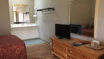 Une chambre d’hôtel comprenant un lit, une commode en bois, un téléviseur à écran plat, un miroir et une salle de bain avec un lavabo et un miroir.
