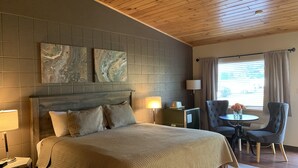 A hotel room with a large bed, a wooden ceiling, a gray tiled wall, and a window with curtains.