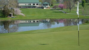 A golf course with a pond, a clubhouse, and a building with a green roof.