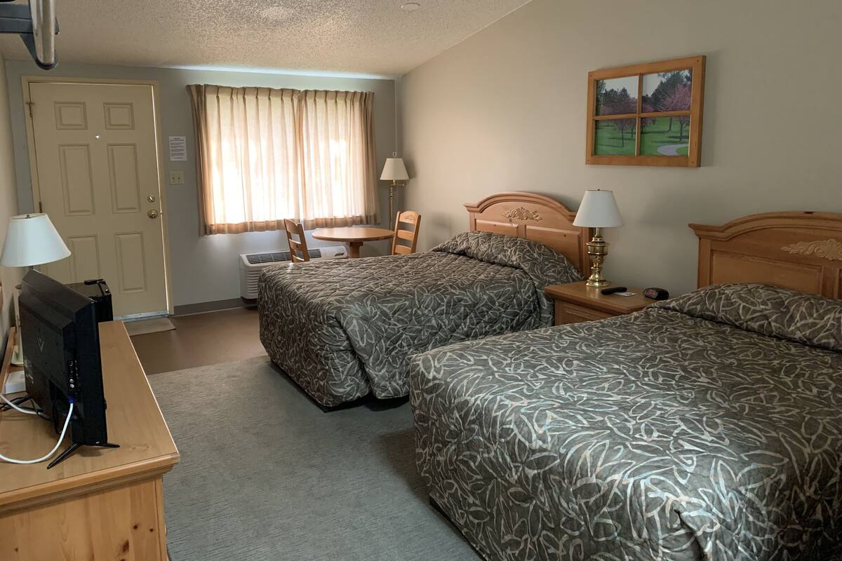 A hotel room with two beds, a desk with a computer, a chair, a lamp, and a painting on the wall.