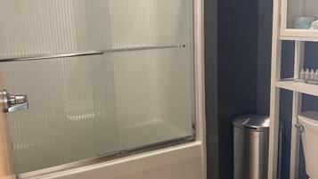 Une salle de bain avec une douche à parois de verre, des toilettes blanches et une petite poubelle.
