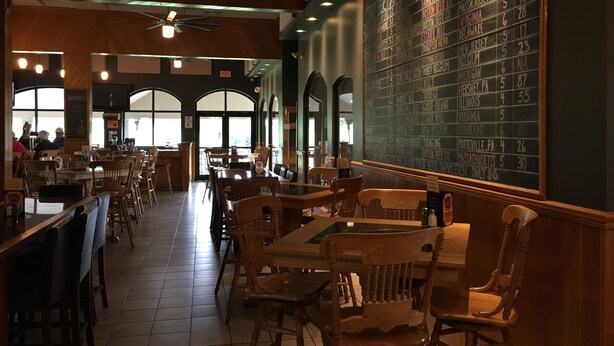 A restaurant with wooden furniture, a chalkboard menu, and large windows.