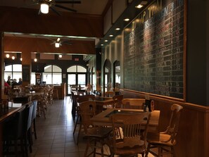 Un restaurante con muebles de madera, un menú en pizarra y ventanas amplias.