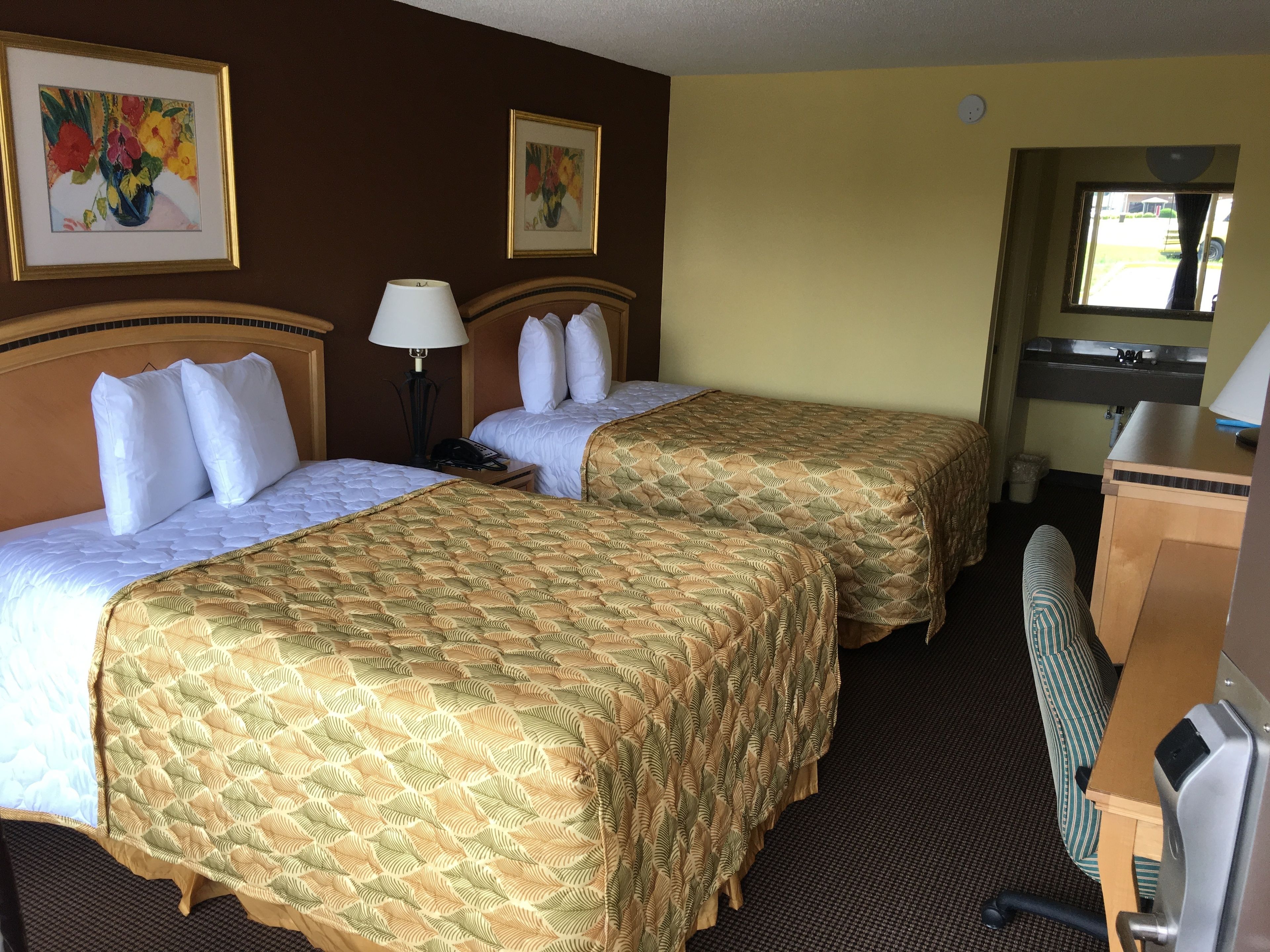 A hotel room with two beds, a desk, a chair, and a window.