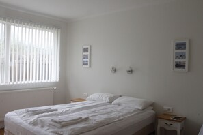 Une chambre avec un grand lit, une table de chevet et une fenêtre avec des stores.