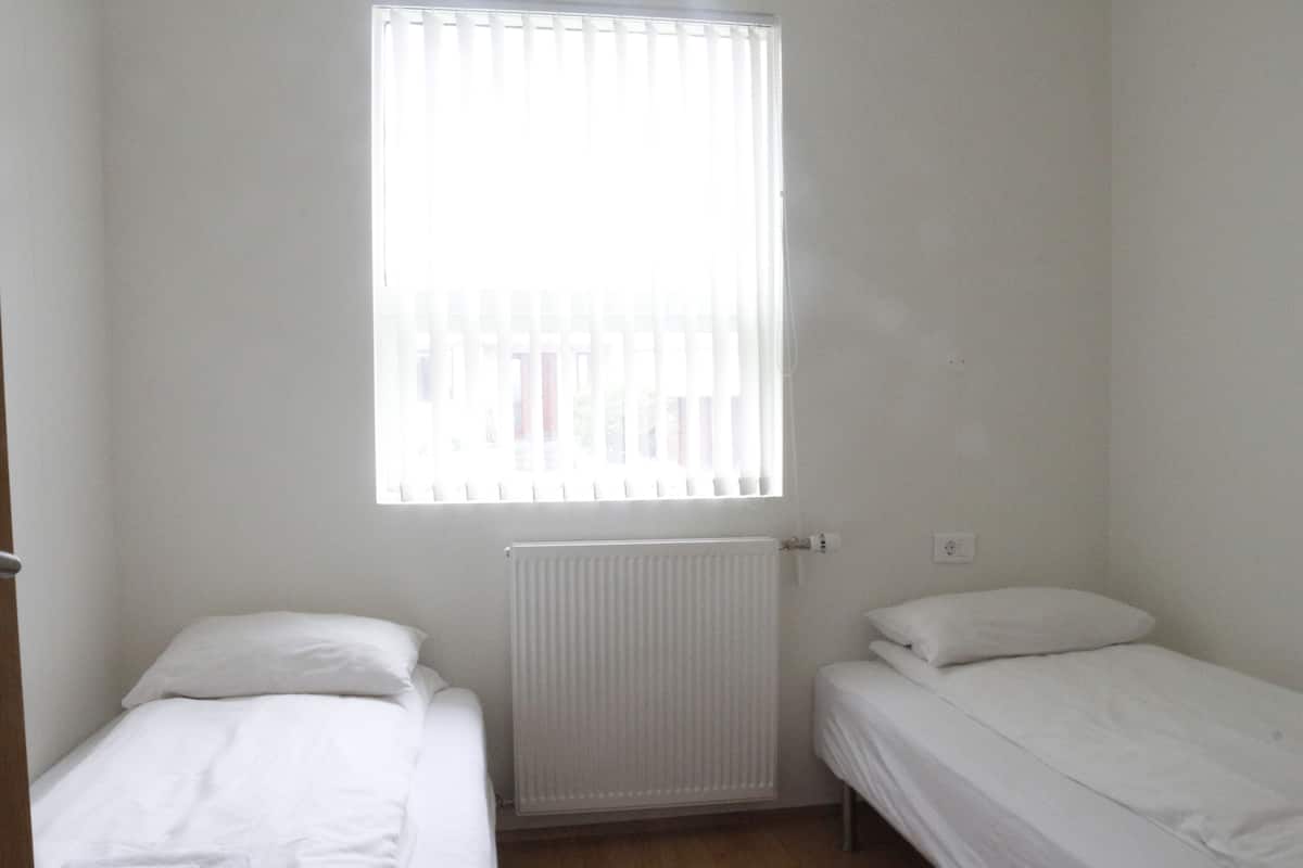 Ein kleines Zimmer mit einem Einzelbett, einem Fenster und einer Heizung.
