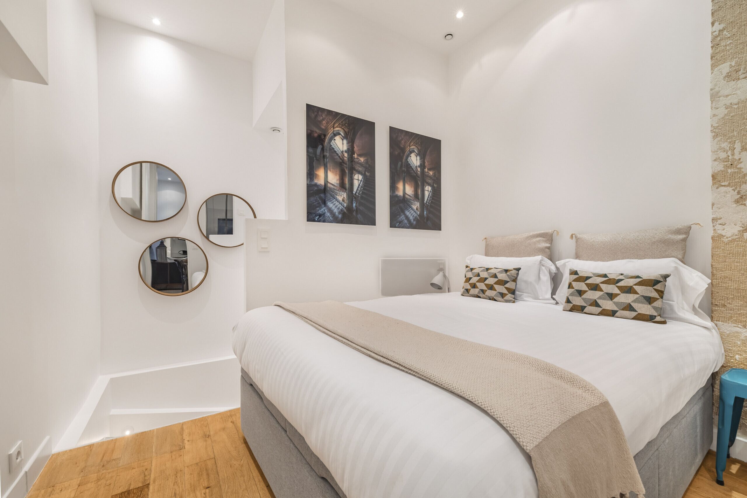 A bedroom with a large bed, two wall-mounted mirrors, and two framed pictures.