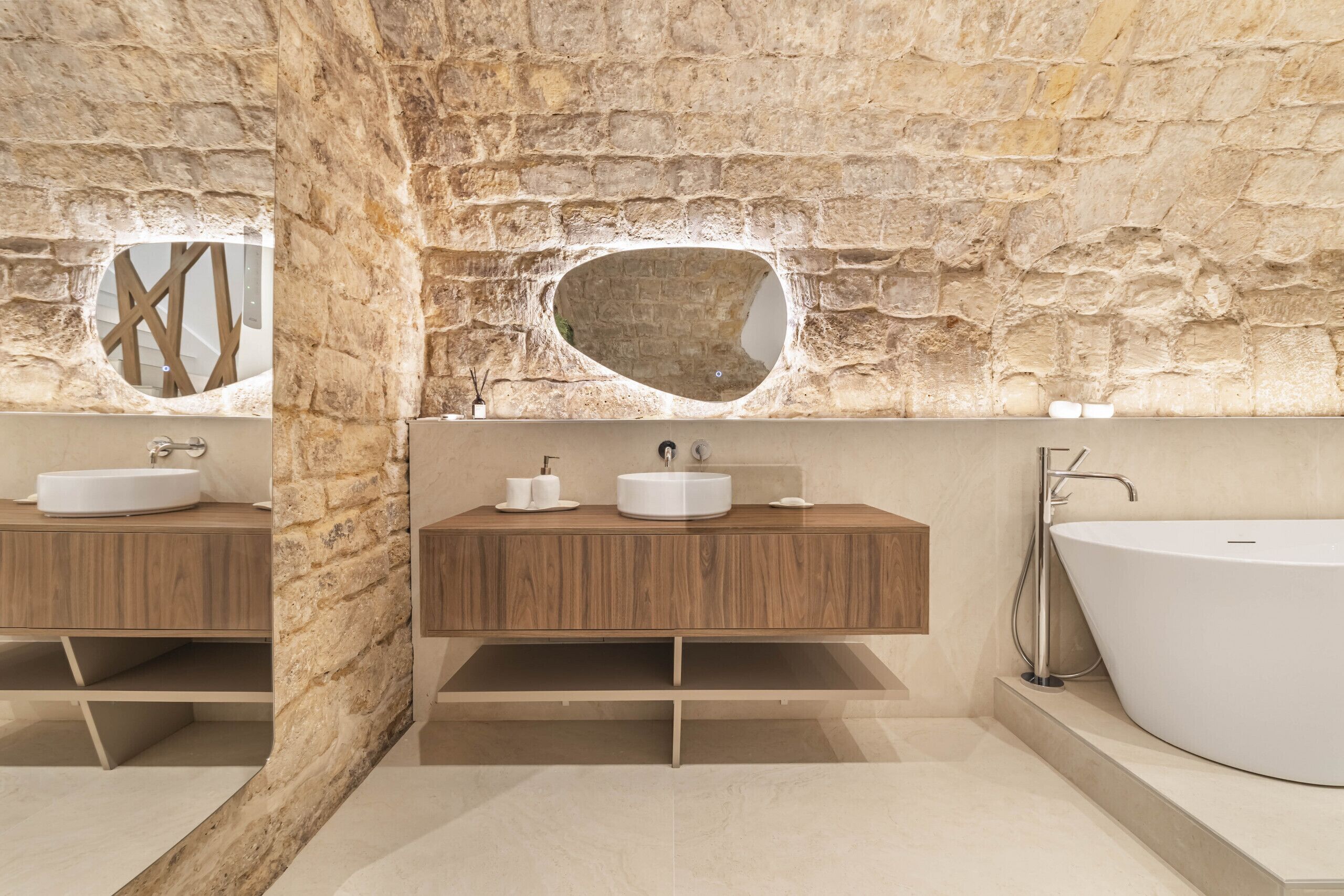 A modern bathroom with a stone wall, two sinks, and a freestanding bathtub.