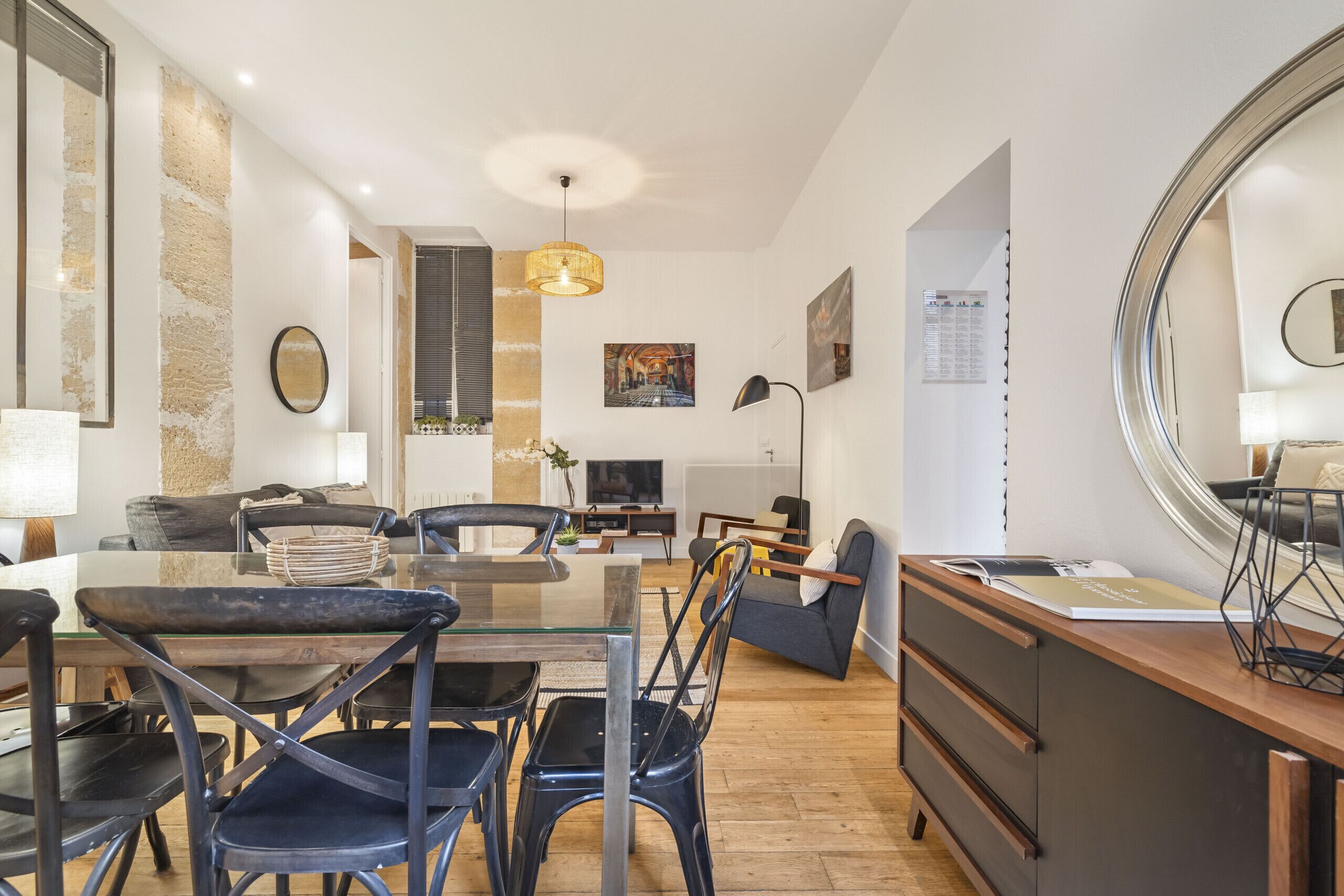 Un salon moderne avec une table à manger en verre, des chaises noires, un canapé et un téléviseur.