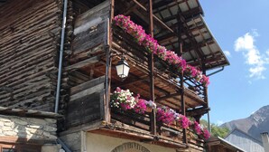 Een rustiek houten gebouw met een stenen fundering, een houten balkon met bloembakken en een traditionele houten deur.