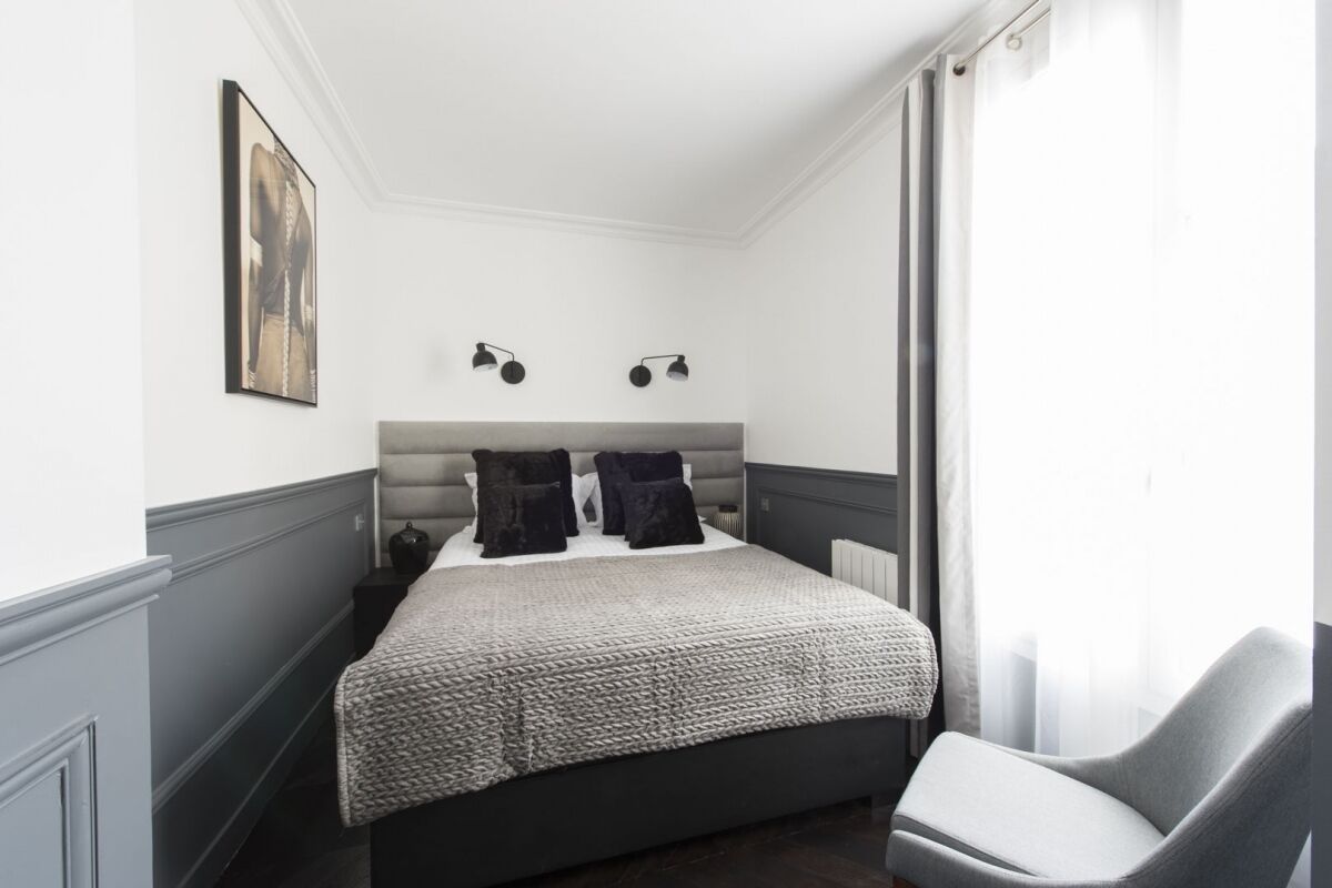 Une chambre à coucher comprenant un lit, une chaise, un tableau accroché au mur et deux lampes fixées au mur.