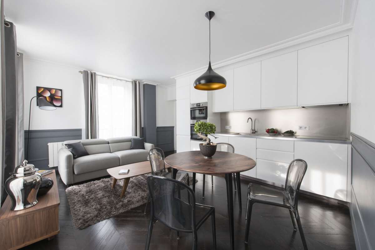 Ein modernes Wohnzimmer mit grauem Sofa, einem runden Holztisch und einer hängenden Pendelleuchte.