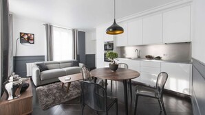 A modern living room with a grey sofa, a round wooden table, and a hanging pendant light. - Black Pearl, 1BR/1BA, 3 people (París)