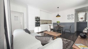 A modern living room with a grey sofa, a wooden coffee table, and a dining area with a small table and chairs. - Black Pearl, 1BR/1BA, 3 people (París)