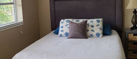 Ein ordentlich gemachtes Bett mit weißer Steude, dunklem Kopfteil und dekorativen Kissen.