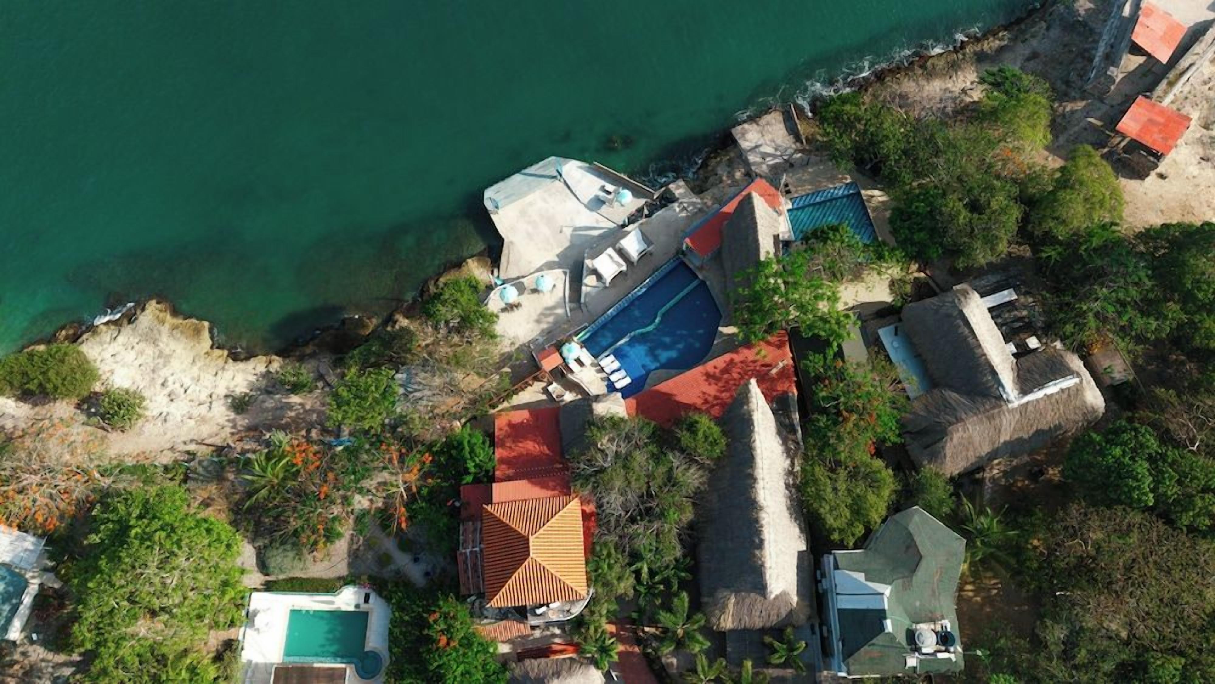 An aerial view of a coastal property with multiple buildings, a swimming pool, and a beach area.