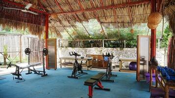 A covered outdoor gym with exercise equipment, a stone wall, and a bench.