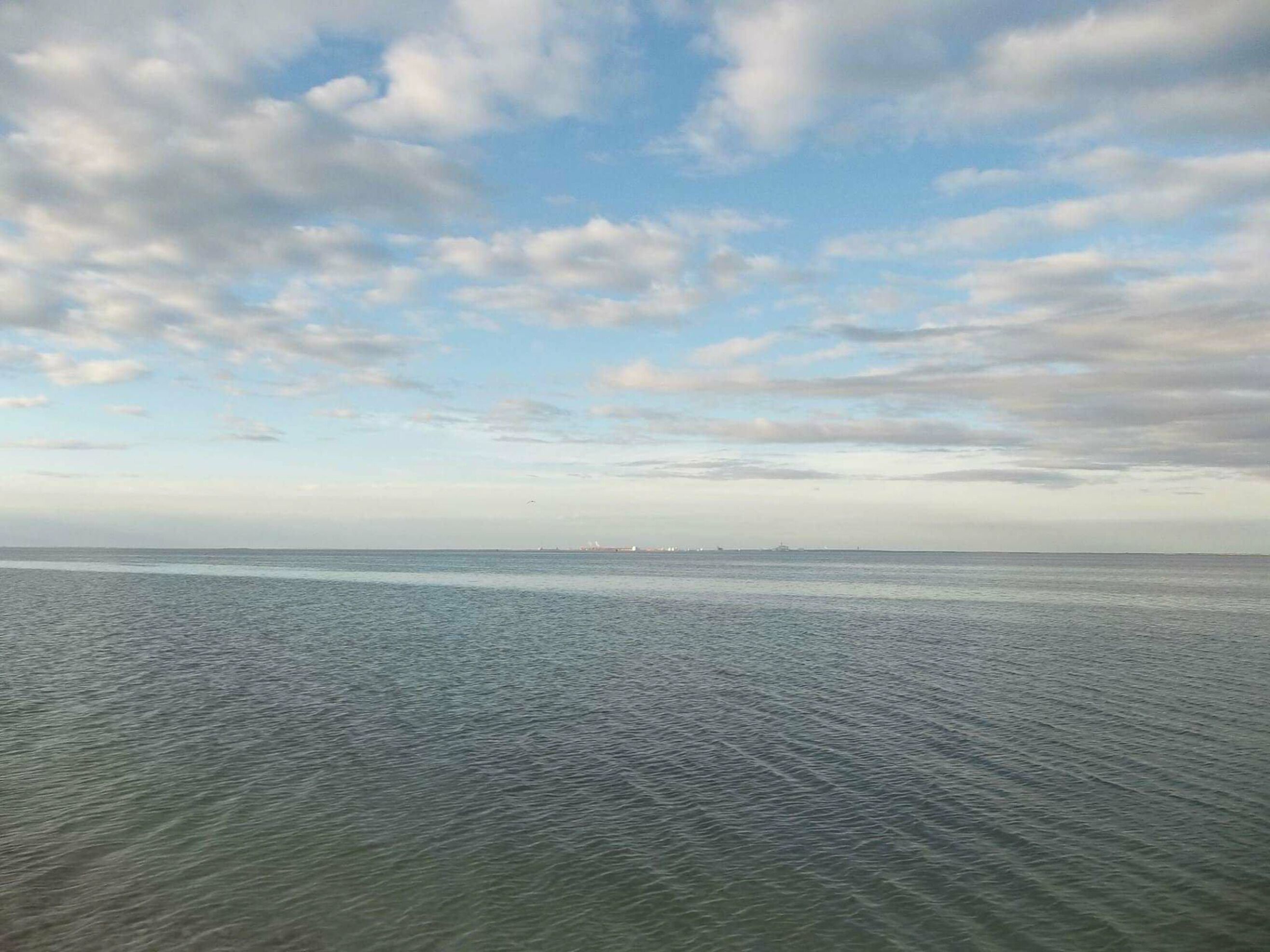 Ruhiges Meer mit einer entfernten Küste und einem teilweise bewölkten Himmel.
