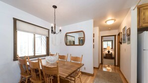 A dining area with a wooden table and chairs, a chandelier, a mirror, and a view into the kitchen. - Outpost: Sleeping Indian E12 - Air Conditioning! (Teton Village)