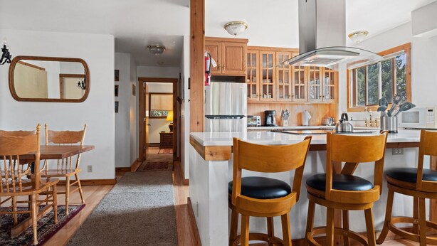 A modern kitchen with wooden cabinets, a central island, and bar stools. - Outpost: Sleeping Indian E12 - Air Conditioning! (Teton Village)