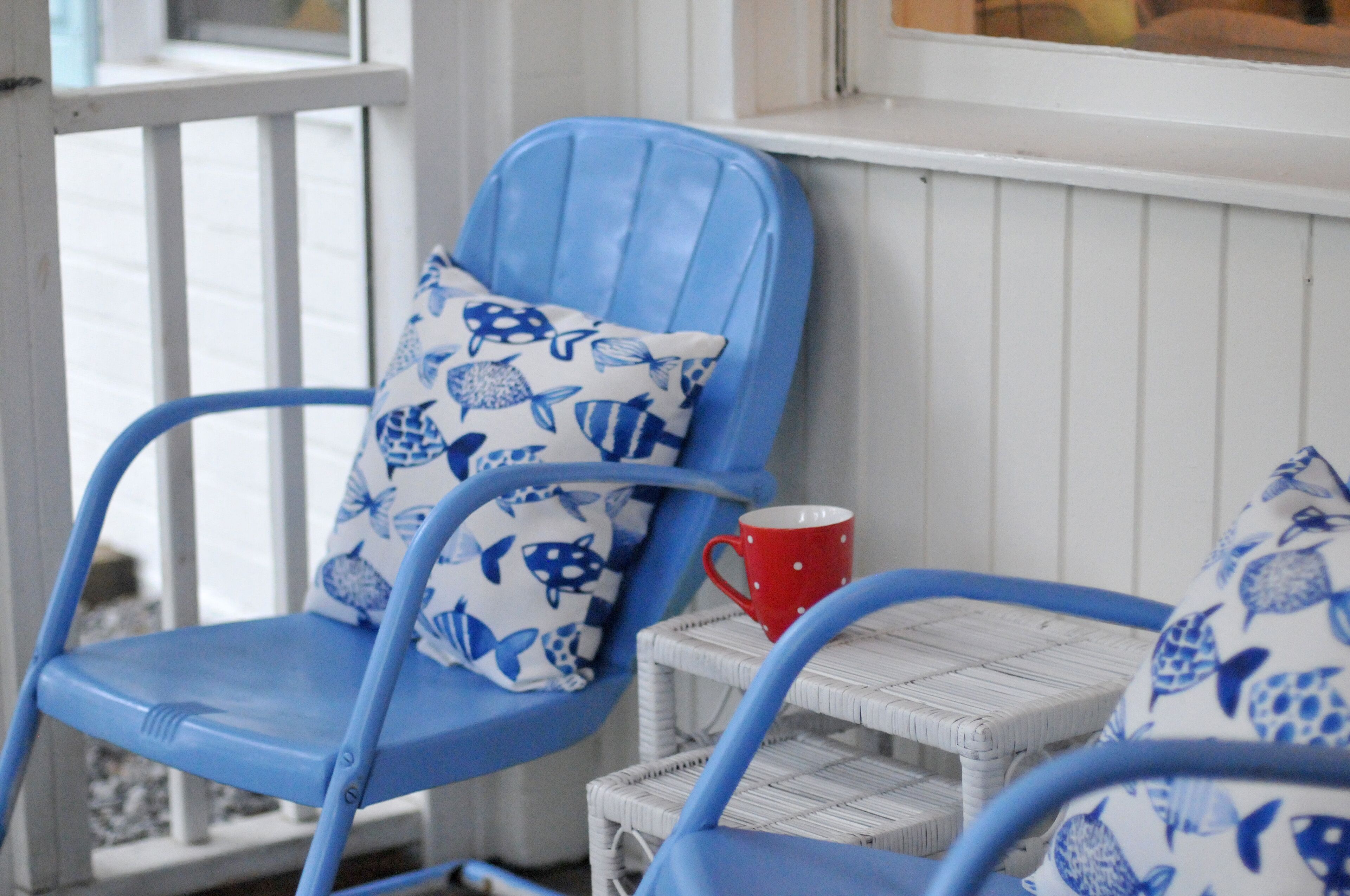 A blue chair with a white cushion featuring blue fish patterns, a red mug, and a wicker table.