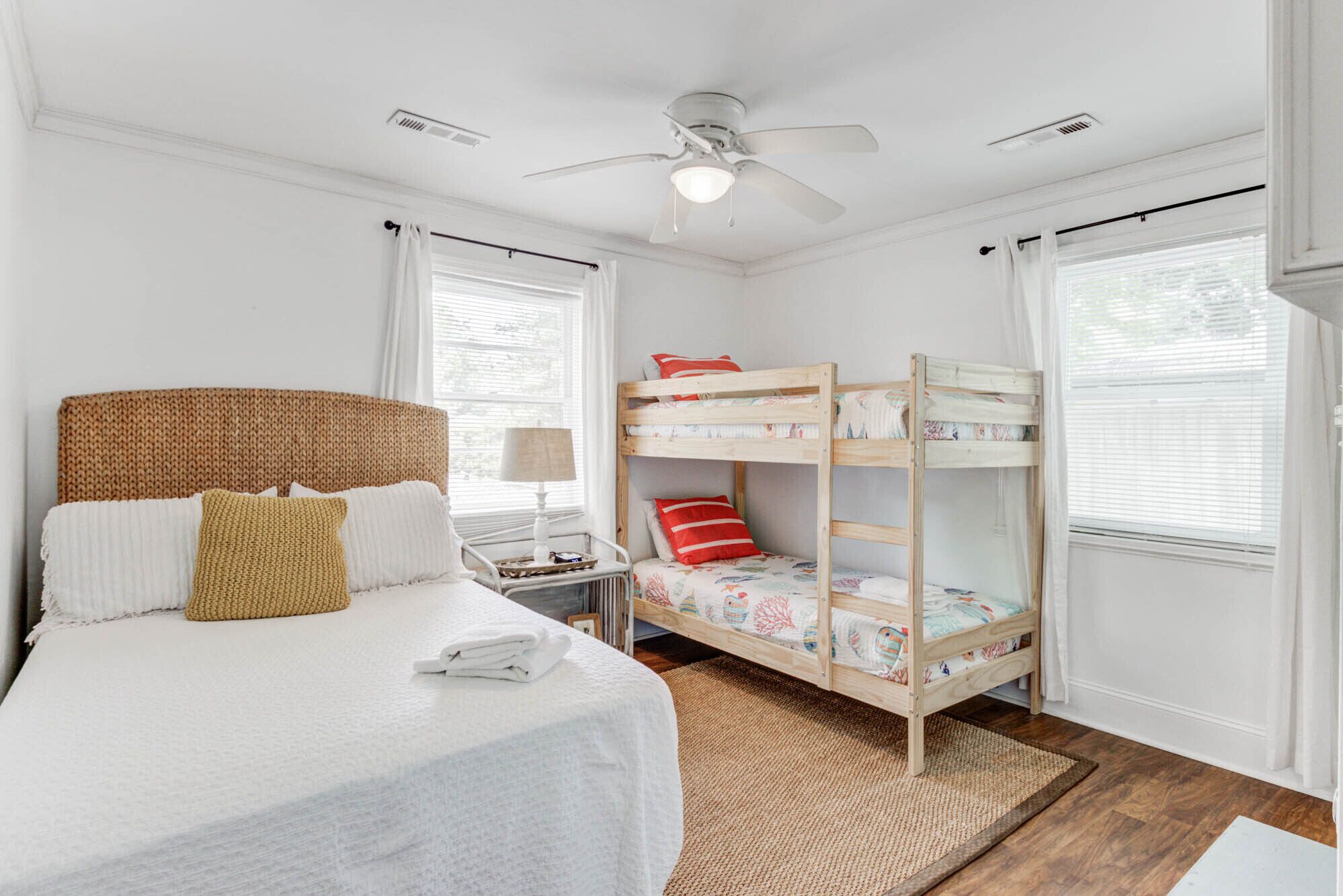 Une chambre avec un lit superposé, un lit simple, un ventilateur de plafond et une fenêtre avec des rideaux.