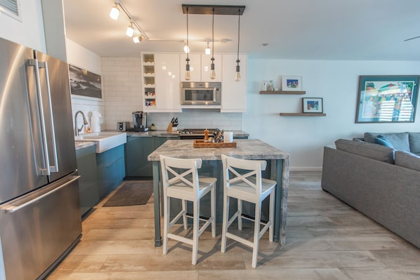Una cocina moderna con una isla central, electrodomésticos de acero inoxidable y un sofá gris en la sala de estar.