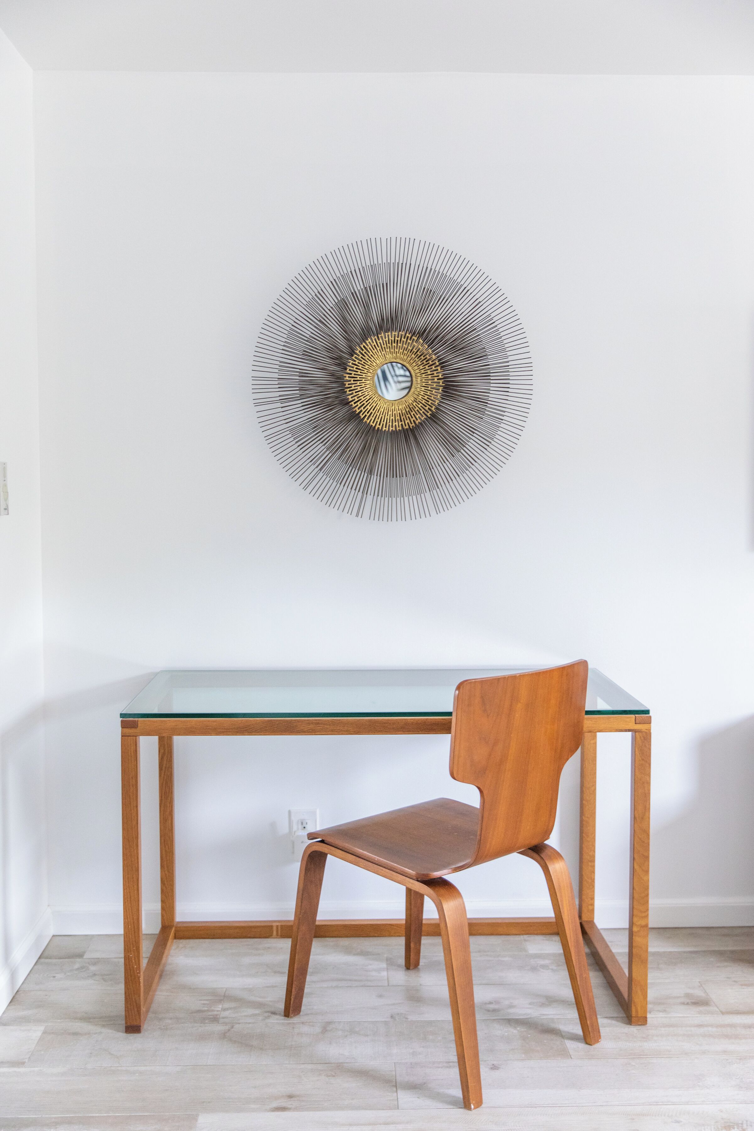 A modern room with a glass-top table, a wooden chair, and a wall-mounted abstract art piece.