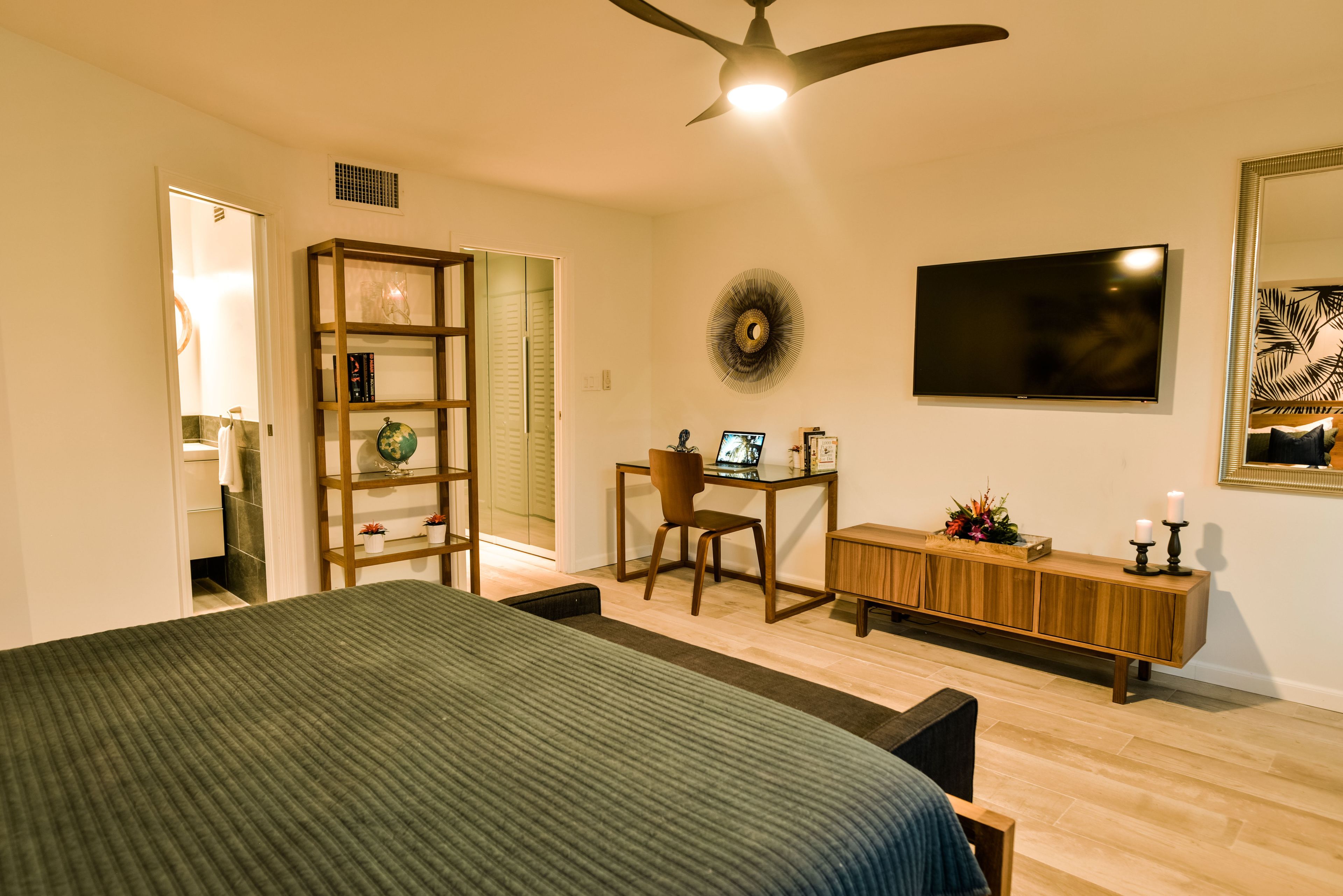 A bedroom with a large bed, a desk with a chair, a TV, and a cabinet with decorative items.