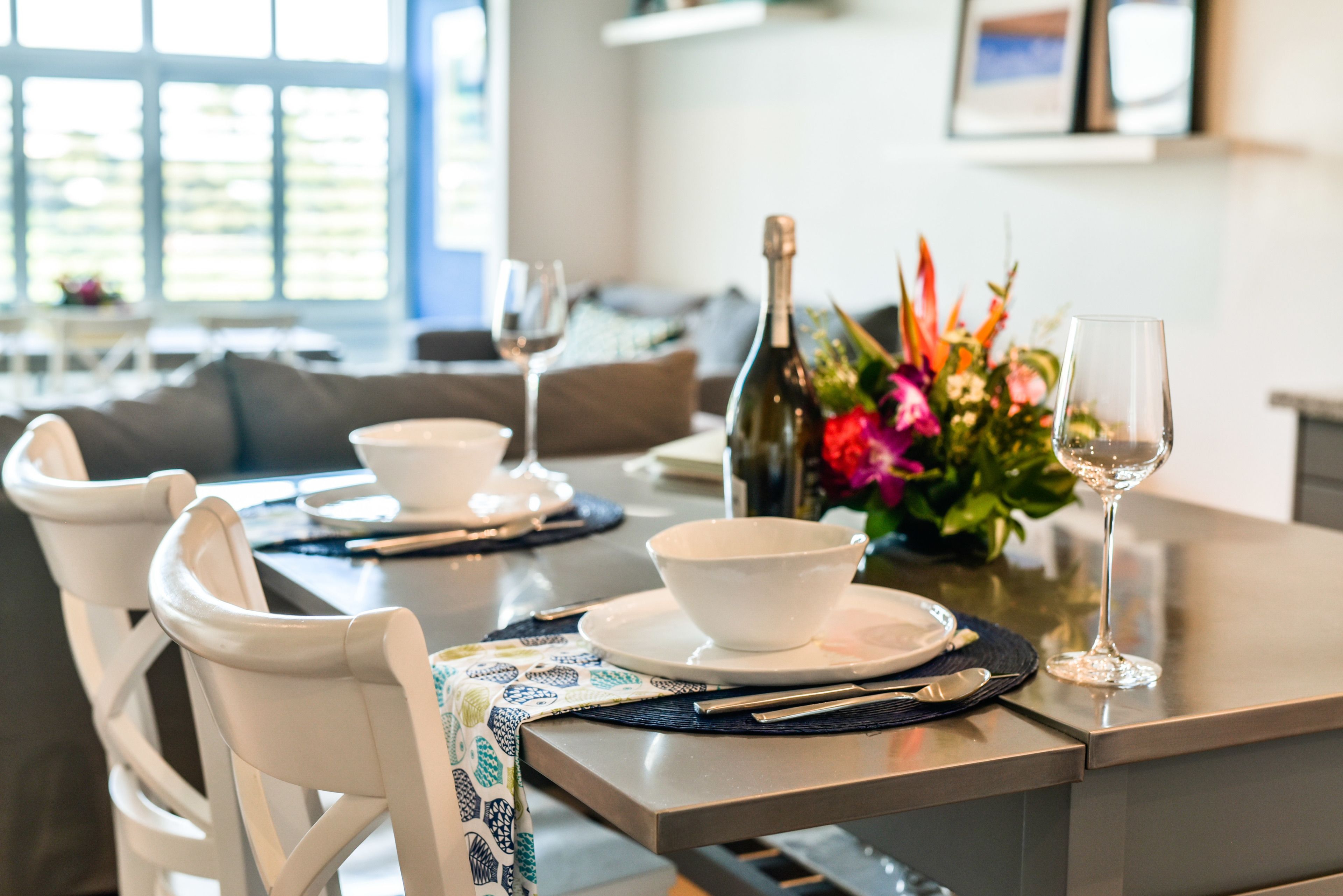 A dining table set with white bowls, a bottle of wine, and a glass on a table with a woven placemat.