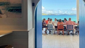 A group of people dining at a table with a view of the sea through an arched doorway. - Beachfront Villas at Crystal Cove (St. Thomas)
