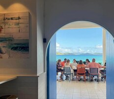 Un grupo de personas cenando en una mesa con vista al mar a través de un arco.