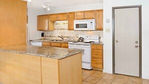 A kitchen with wooden cabinets, a granite countertop, a white stove, and a microwave.