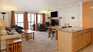 A modern living room with a sofa, coffee table, and chairs, a kitchen area with a large island and cabinets, and a fireplace.