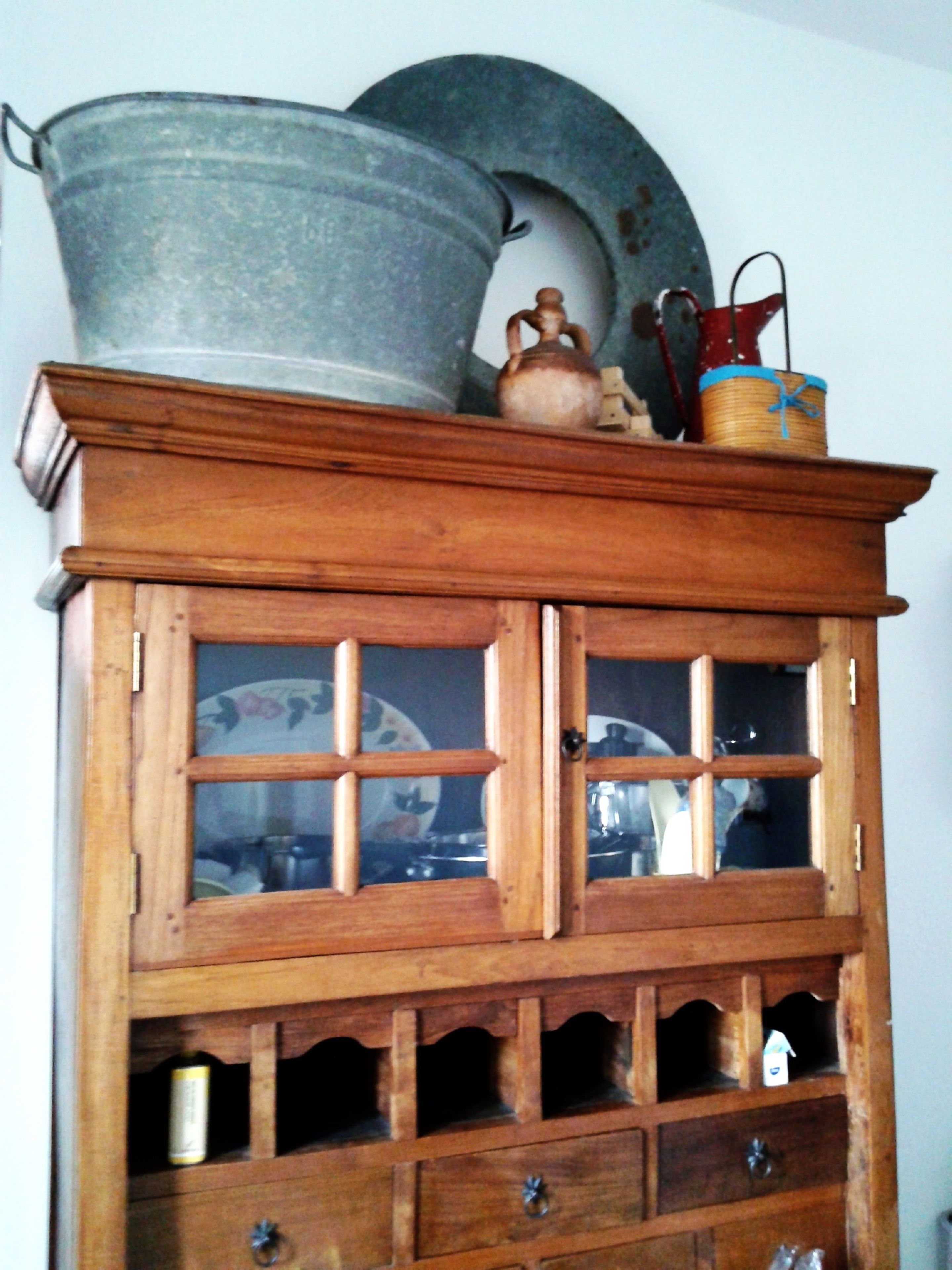 Un armario de madera con varios cajones y puertas de cristal, que contiene distintos utensilios de cocina.