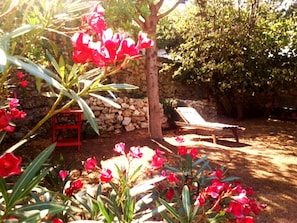 Um jardim com flores vermelhas, um muro de pedra e uma cadeira de descanso de madeira.