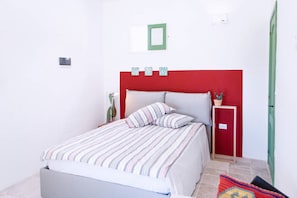 Quarto com cama, mesa de cabeceira, planta em vaso e cabeceira vermelha.