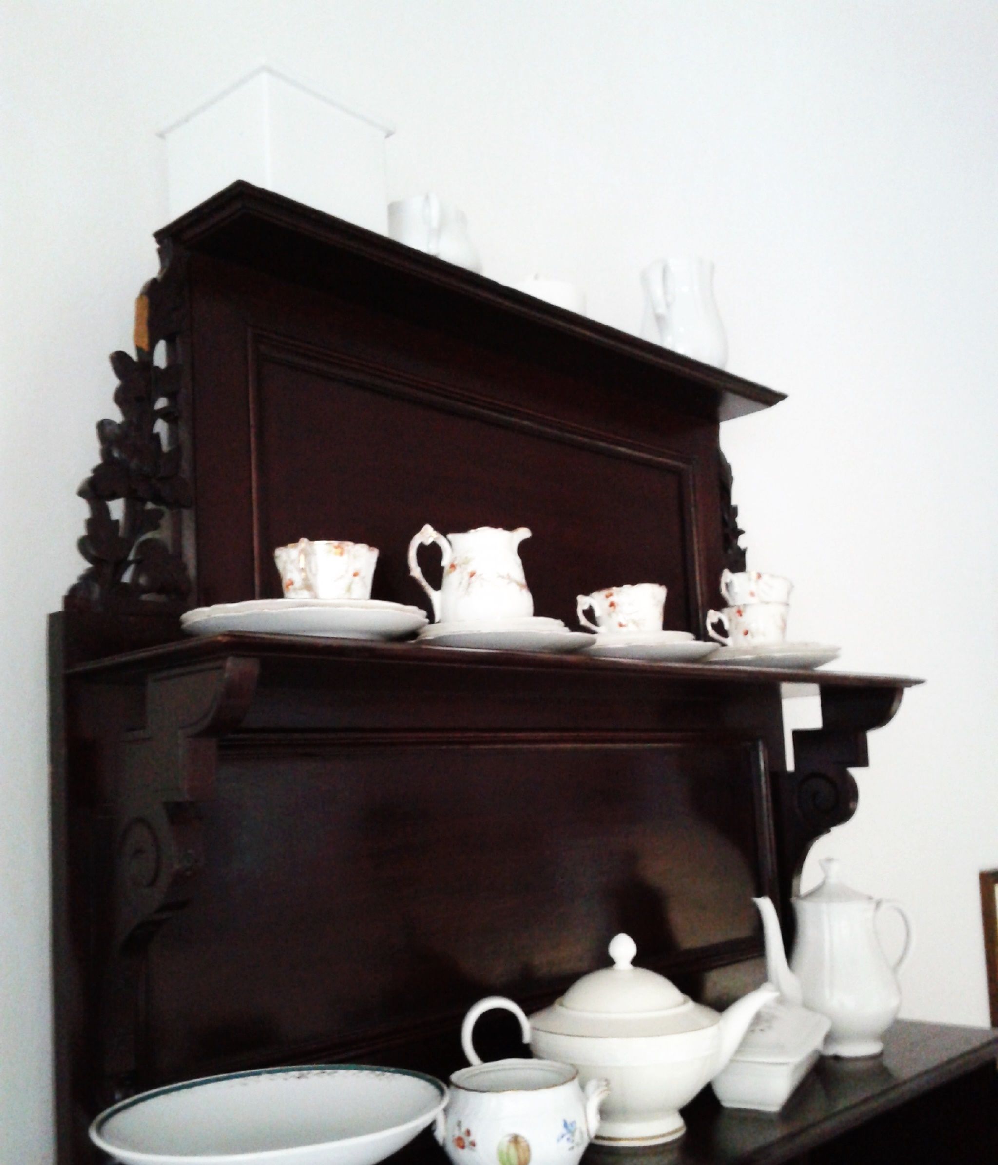 A dark wooden cabinet with white ceramic tea sets and cups.