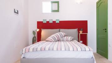 Un dormitorio con cama, cabecera roja, mesita de noche con lámpara y puerta verde.