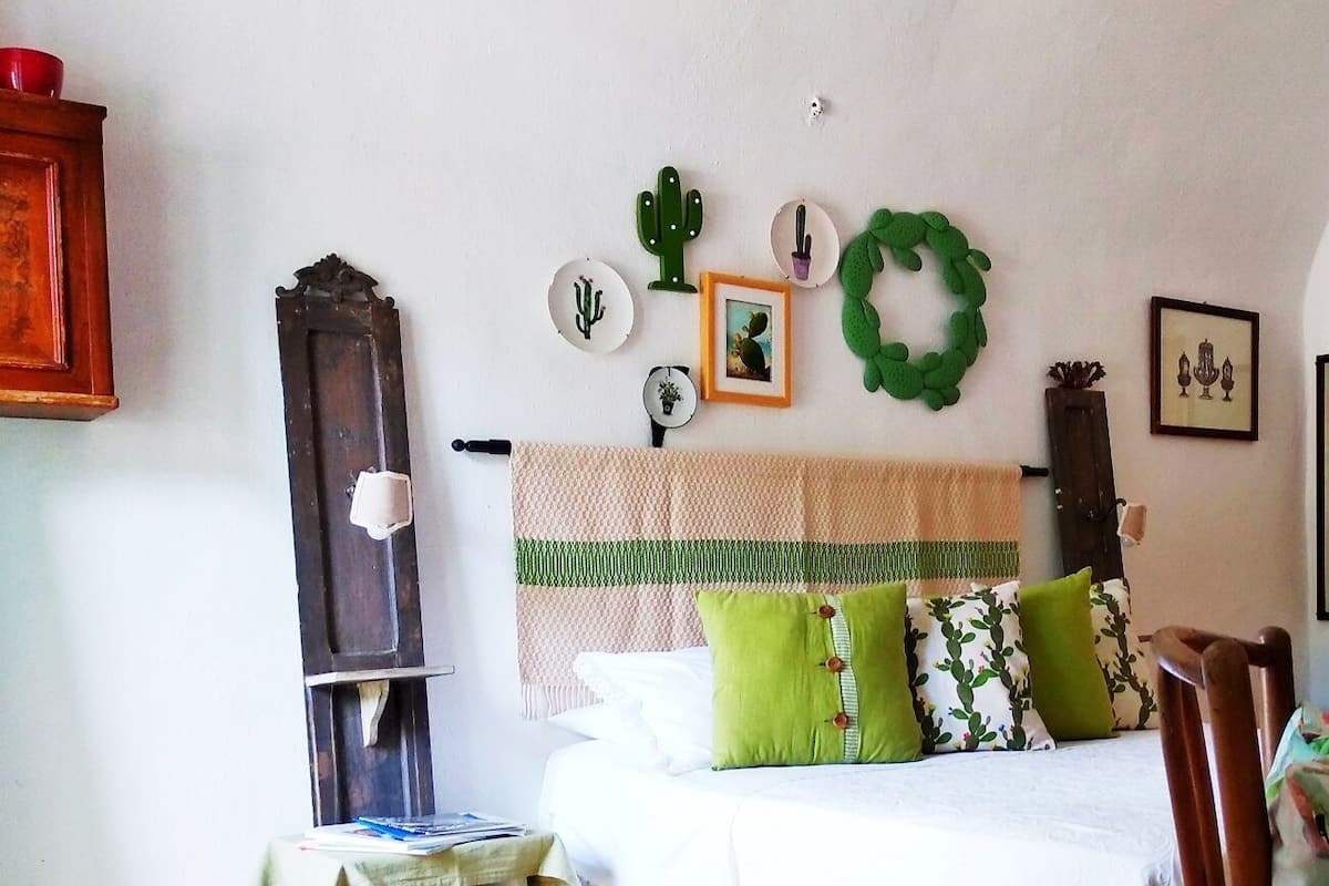 Un dormitorio con una cama, almohadas, una colcha y adornos en la pared, incluyendo cactus y un arreglo floral.