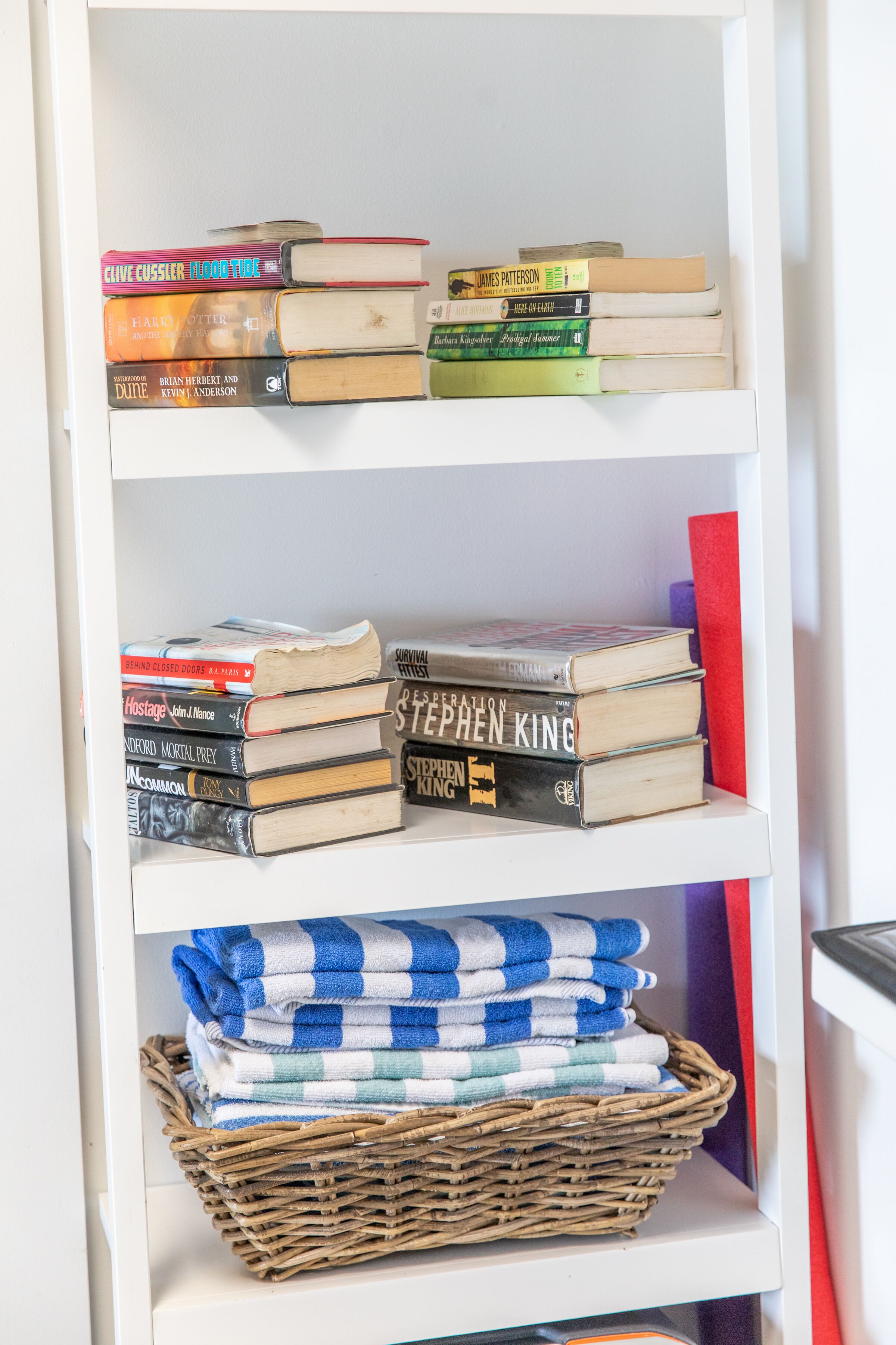 Una estantería con libros y una cesta de toallas dobladas.