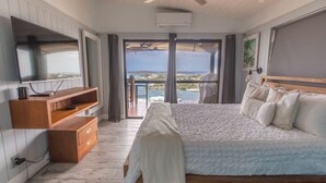 A bedroom with a large bed, a TV, a wooden dresser, and a balcony with a view. - Villa Marina Vista (St. Thomas)