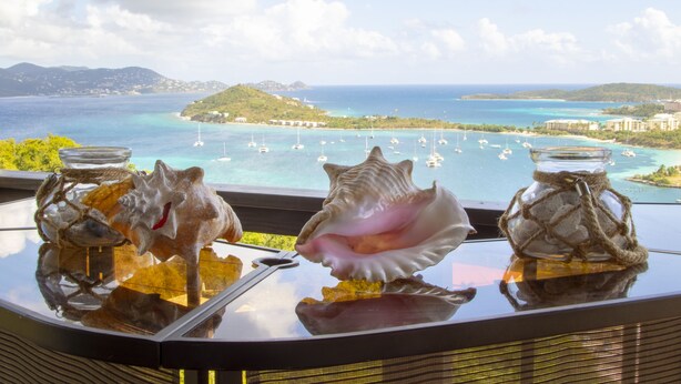 A table with three glass jars containing seashells, overlooking a coastal view with boats and buildings. - Villa Marina Vista (St. Thomas)