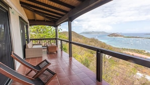 A balcony with a view of the sea, a wicker sofa, and a wooden chair. - Villa Marina Vista (St. Thomas)