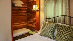 A small, cozy room with a wooden wall, a bed with green patterned pillows, a bedside table with a lamp, and a bench. - Romantic Inn suite with Air Jet Jacuzzi & private bath (Logan)